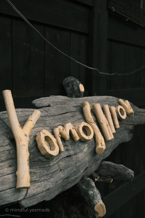 Driftwood letters spelling 'Yomoshirou' on a dark background
