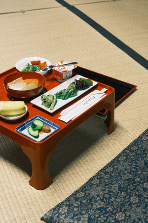 Traditional Japanese meal on a wooden tray with various dishes on a tatami mat floor.