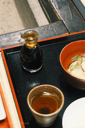 Bowl of soup with a bottle and cup on a wooden tray