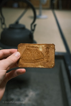 Hand holding a brown biscuit with gassho thatched roof house imprint