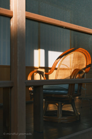 Wicker chair by a table with sunlight filtering through, creating a warm glow.
