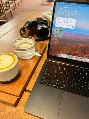 Laptop on a wooden table with a camera, glass of water, and cup of coffee.