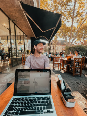 Man sitting at a table with a laptop in an outdoor cafe setting