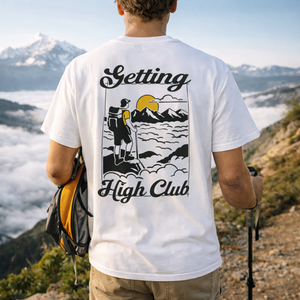 Person wearing a white t-shirt with 'Getting High Club' hiking design in a mountainous landscape