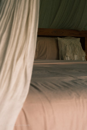 Bed with beige bedding and a canopy in a softly lit room
