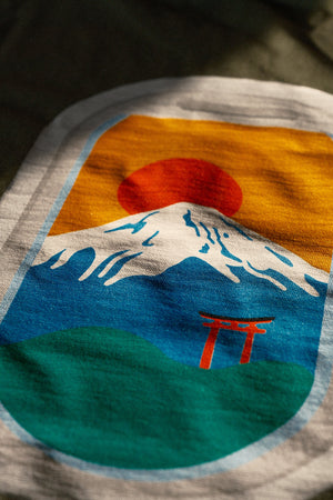 Close-up of a t-shirt with a colorful Mount Fuji and Otorii design from airplane window.