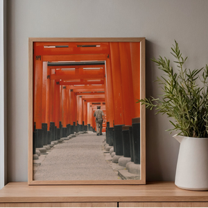 Framed photograph of a person walking through a row of red torii gates on a wooden shelf with a plant.