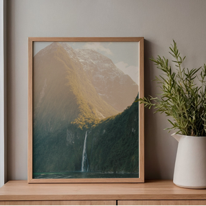 Framed print of a mountain landscape on a wooden shelf with a plant.