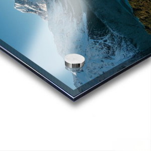 Close-up of a water fountain spout with water spraying out, set against a blue background. Features Mount Cook / Aoraki and nearby lakes in New Zealand.