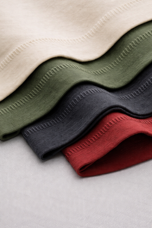 Four folded fabrics in beige, green, black, and red on a light gray background