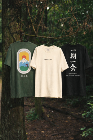 Three t-shirts hanging on a tree branch in a forest setting