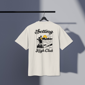 White t-shirt with 'Getting High Club' hiking graphic on a hanger against a gray background