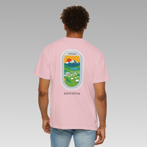 Person wearing a pink t-shirt with a colorful New Zealand mountains, campervan, and sheep graphic on the back against a gray background